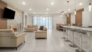 A modern living room with a sofa, a coffee table, and a TV mounted on the wall. - Orlando Escape • 8BR • Jacuzzi, Cinema & Arcade (Davenport)