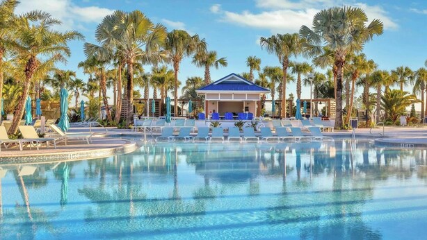 A swimming pool with lounge chairs and umbrellas, surrounded by palm trees. - Orlando Escape • 8BR • Jacuzzi, Cinema & Arcade (Davenport)