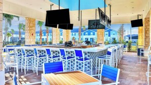 A bar area with white and blue chairs, a wooden bar counter, and multiple flat-screen TVs mounted on the ceiling. - Orlando Escape • 8BR • Jacuzzi, Cinema & Arcade (Davenport)
