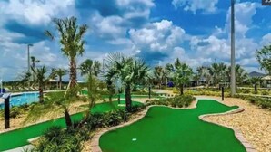 A miniature golf course with a green putting area, sand traps, and palm trees.
