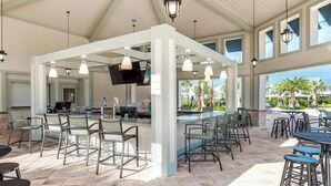 A spacious outdoor bar area with multiple seating arrangements, including bar stools and chairs, under a high ceiling with exposed beams.