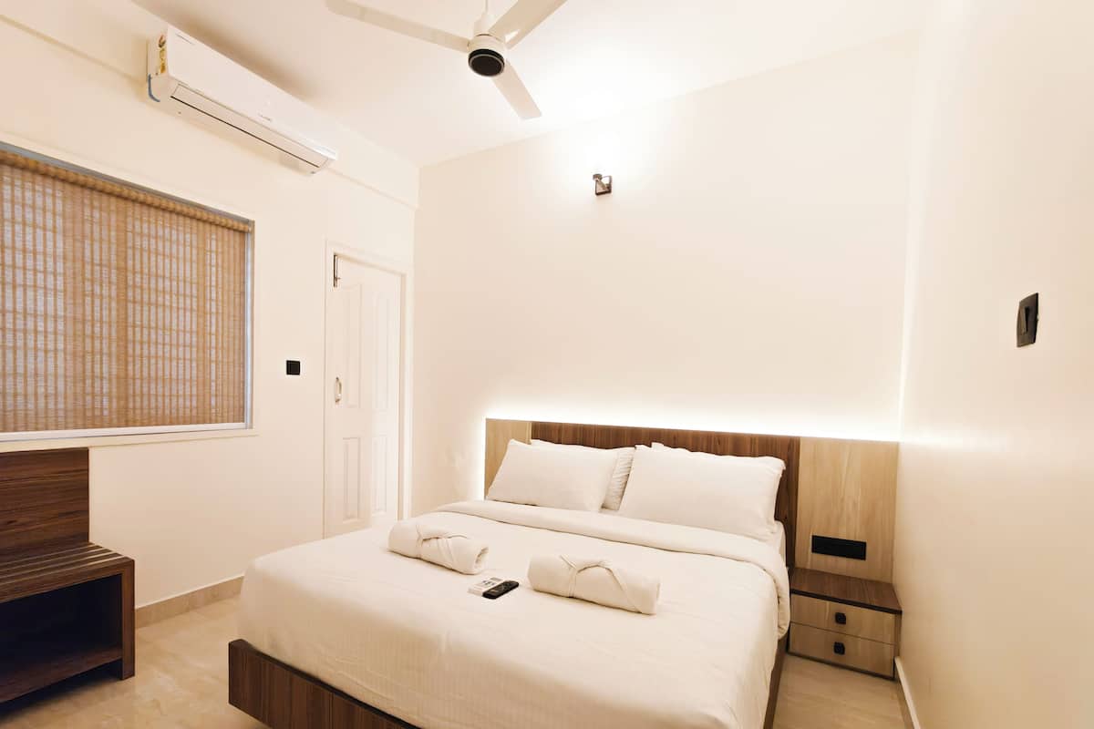 A modern hotel room with a large bed, a wooden headboard, a ceiling fan, and a window with blinds.