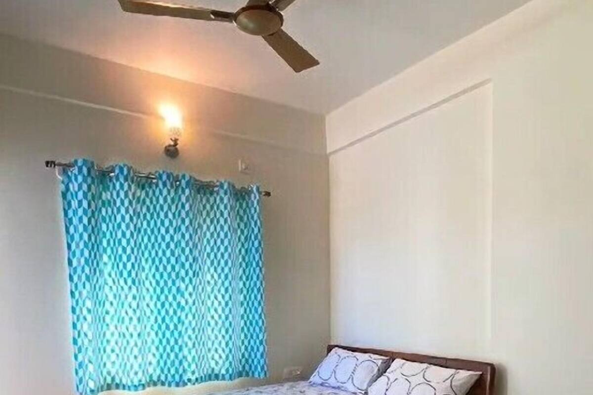A bedroom with a bed, a nightstand, a ceiling fan, and a window with curtains.