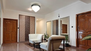 A spacious hallway with a polished marble floor, two white armchairs, a round coffee table, and a large mirror. - Proximus Boutique Hotel Apartments (Bengaluru)