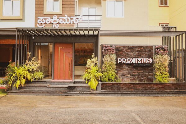 A hotel entrance with a modern facade, a wooden door, and a sign for 'PROXIMUS Boutique Hotel Apartments'.