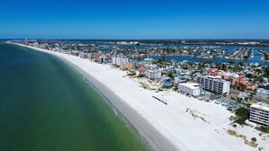 An aerial view of a coastal city with a long sandy beach, dense residential buildings, and a marina with numerous boats.