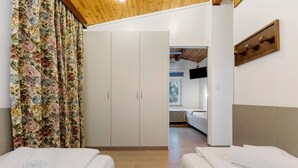 A hotel room with two beds, a wardrobe, a television mounted on the wall, and a wooden ceiling. - Apartment 'Bungalow Pit Stop' with Lake View, Wi-Fi and Air Conditioning (Brenzone sul Garda)