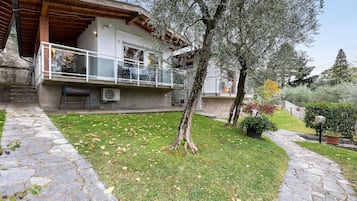 Un vialetto in pietra conduce a una casa con un balcone, immersa in un prato curato e alberi.