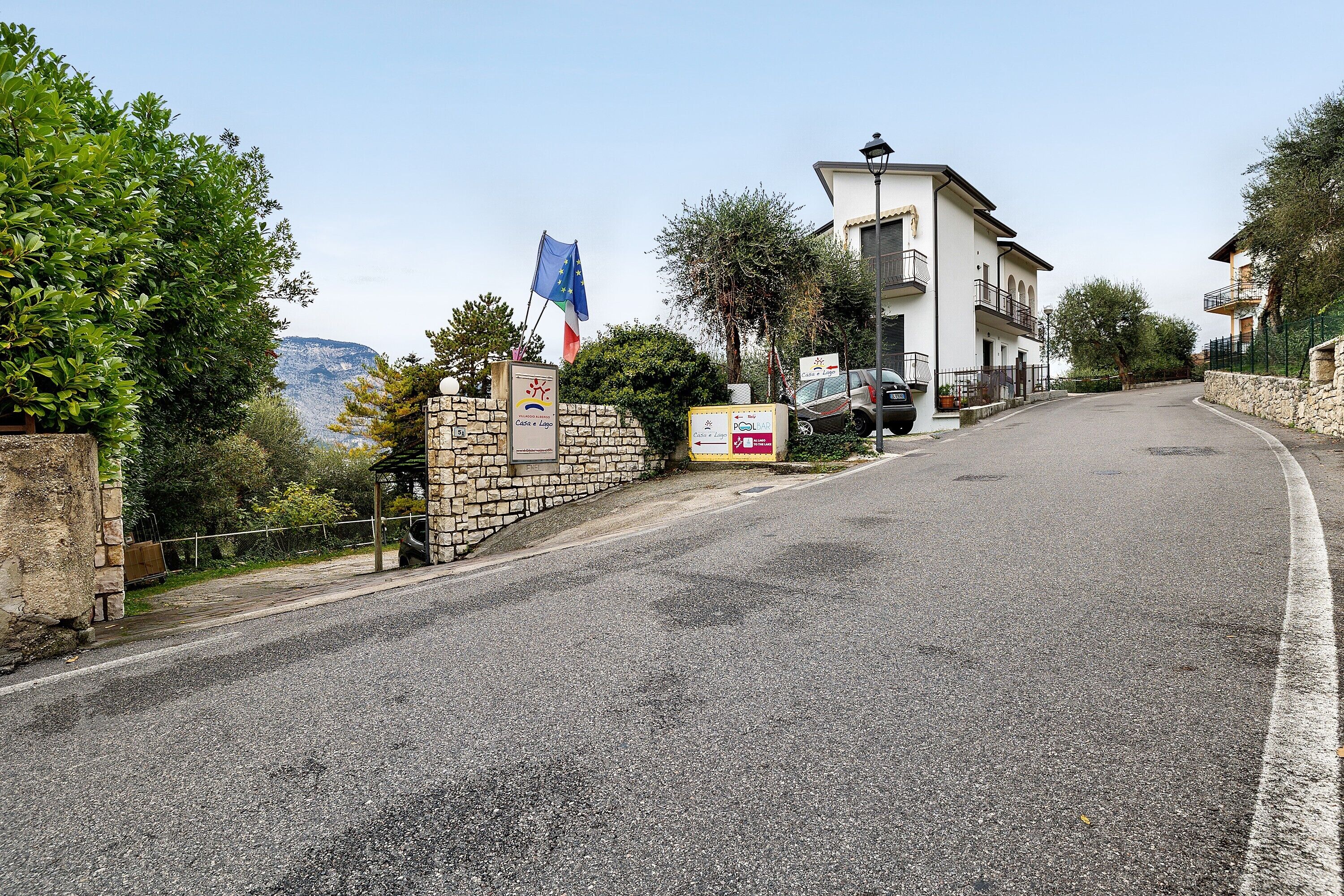 Une route menant à un bâtiment doté d’un mur en pierre, d’un drapeau et d’une enseigne.