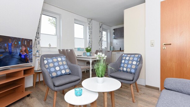 A modern living room with two grey armchairs, a small white table, and a television on a wooden stand. - Wohnung nur 300 m vom Strand in Bensersiel (Bensersiel)