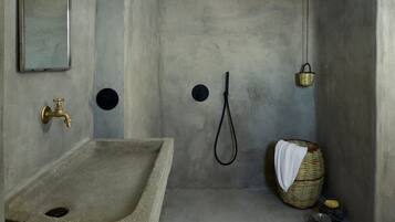 A minimalist bathroom with a stone sink, a mirror, a shower with a handheld showerhead, and a small basket with a towel.