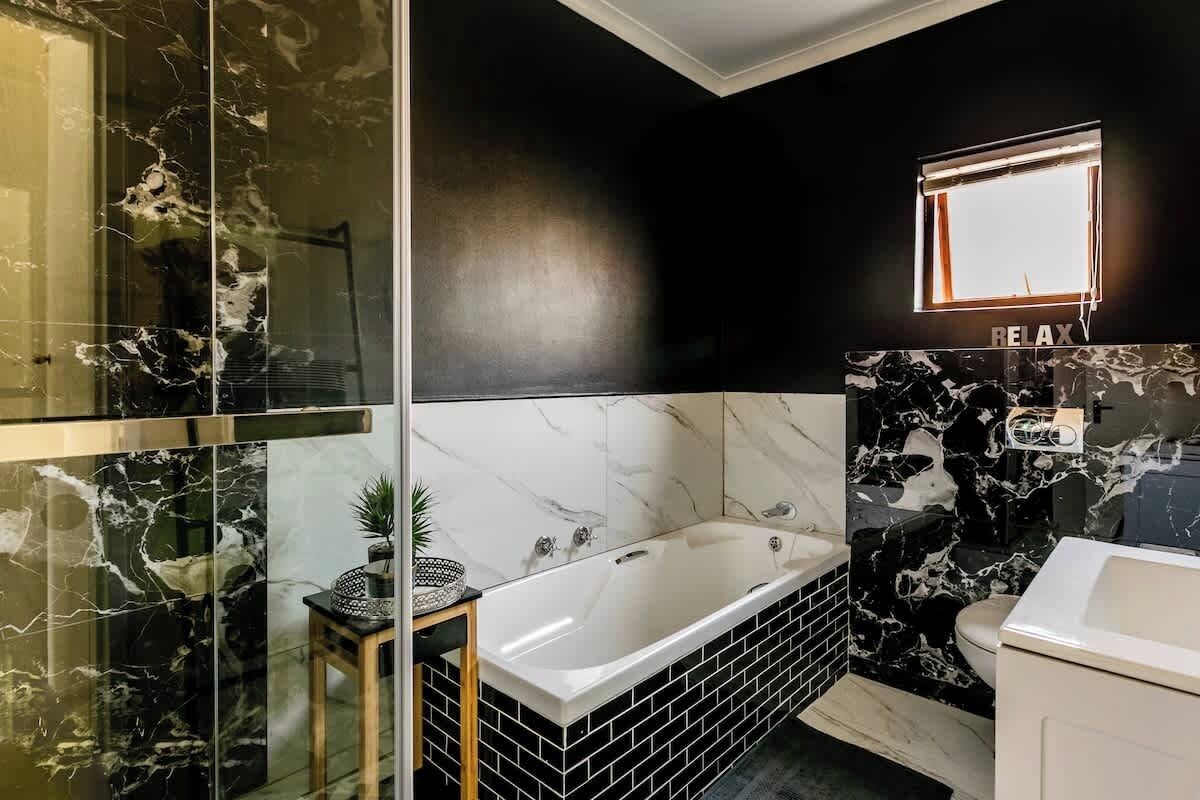 Ein modernes Badezimmer mit einer großen Badewanne, schwarz-weißen Marmorwänden und einem kleinen Holzschemel mit einer Pflanze.
