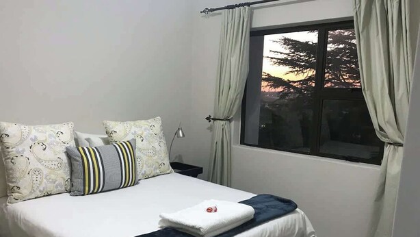 A neatly made bed with a white duvet, two patterned pillows, a striped pillow, and a folded towel.