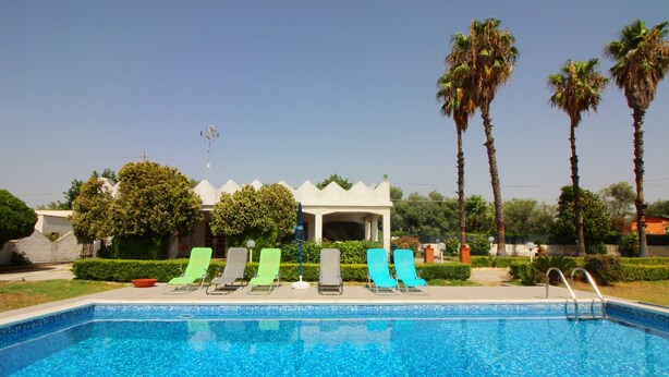 A swimming pool with lounge chairs, a covered seating area, and palm trees in the background. - Typical House with private pool (Siracusa)