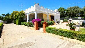A white building with a peaked roof and a balcony, surrounded by greenery and a clear sky. - Typical House with private pool (Siracusa)