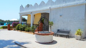 A courtyard with a fountain, a bench, and a building with a white exterior and a wavy roof design. - Typical House with private pool (Siracusa)