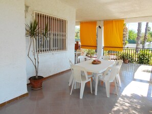 Un patio con una mesa y sillas blancas, una planta en maceta y cortinas amarillas.