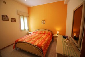 Un dormitorio con cama, mesita de noche, lámpara y espejo.