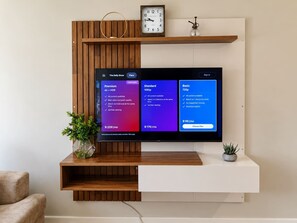 A flat-screen TV mounted on a wooden wall with a clock above it. - Quiet Garden Apartment | Heart of Sandton (Sandton)