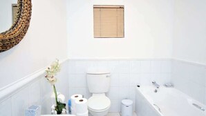 Un baño con inodoro, bañera y una pequeña ventana sobre el inodoro.
