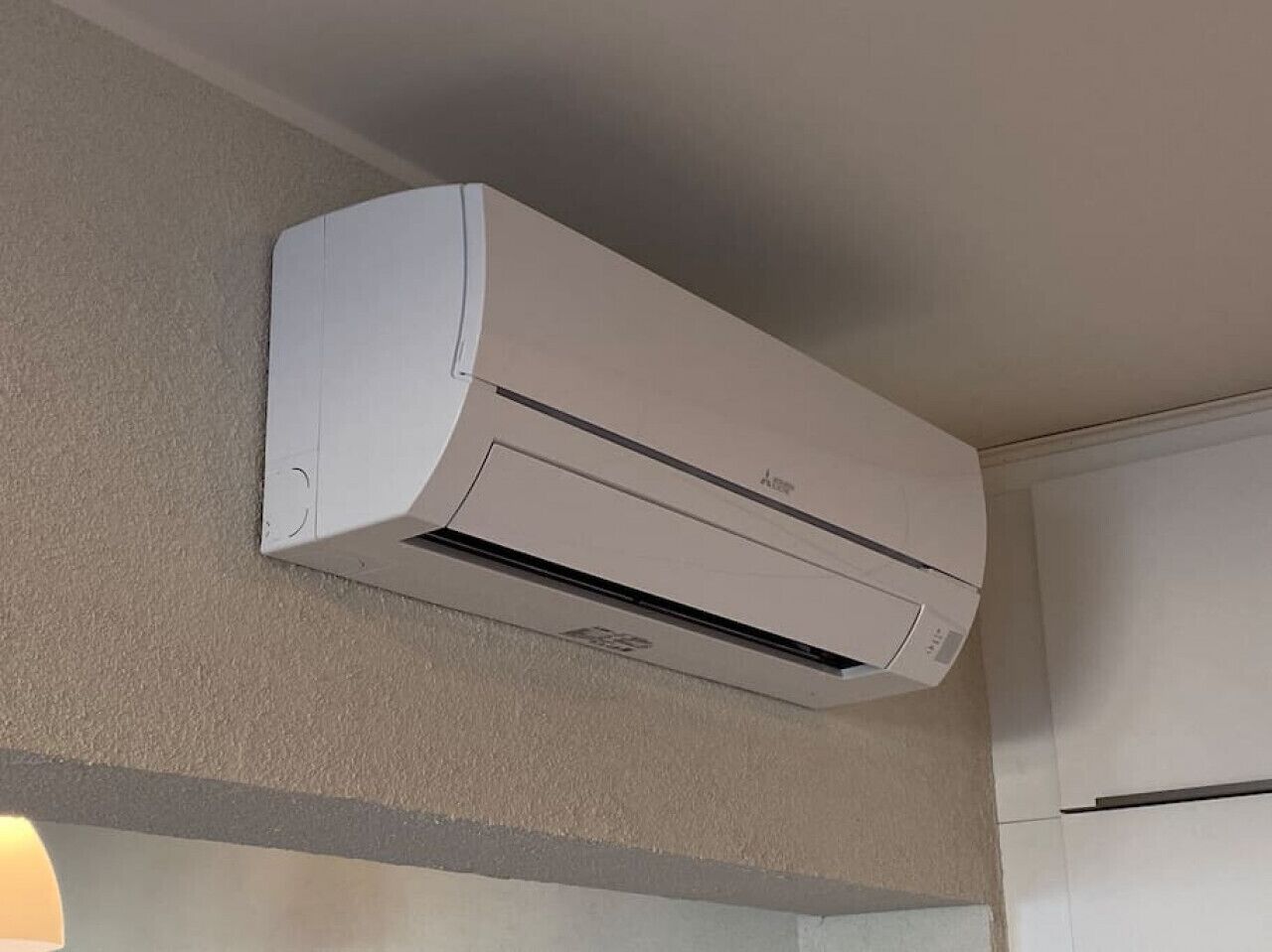 Een wit, aan de muur bevestigd airco-apparaat in een kamer met een effen muur en een deur aan de rechterkant.