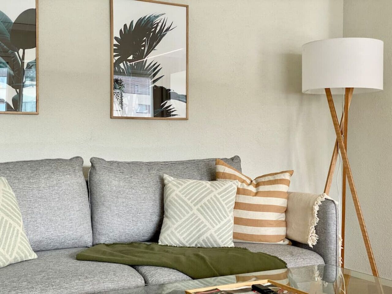 A living room with a grey sofa, patterned cushions, a green throw, and a floor lamp.