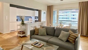 Una sala de estar moderna con un sofá gris, una mesa de centro de cristal y una cocina al fondo.