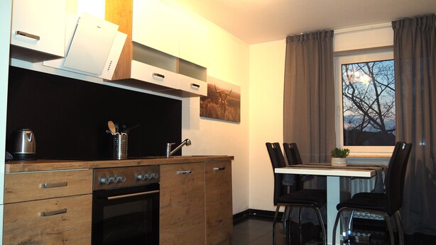 A modern kitchen with wooden cabinets, a built-in oven, and a dining area with a table and chairs. - Central apartment with secure private parking in the backyard (Ludwigshafen am Rhein)