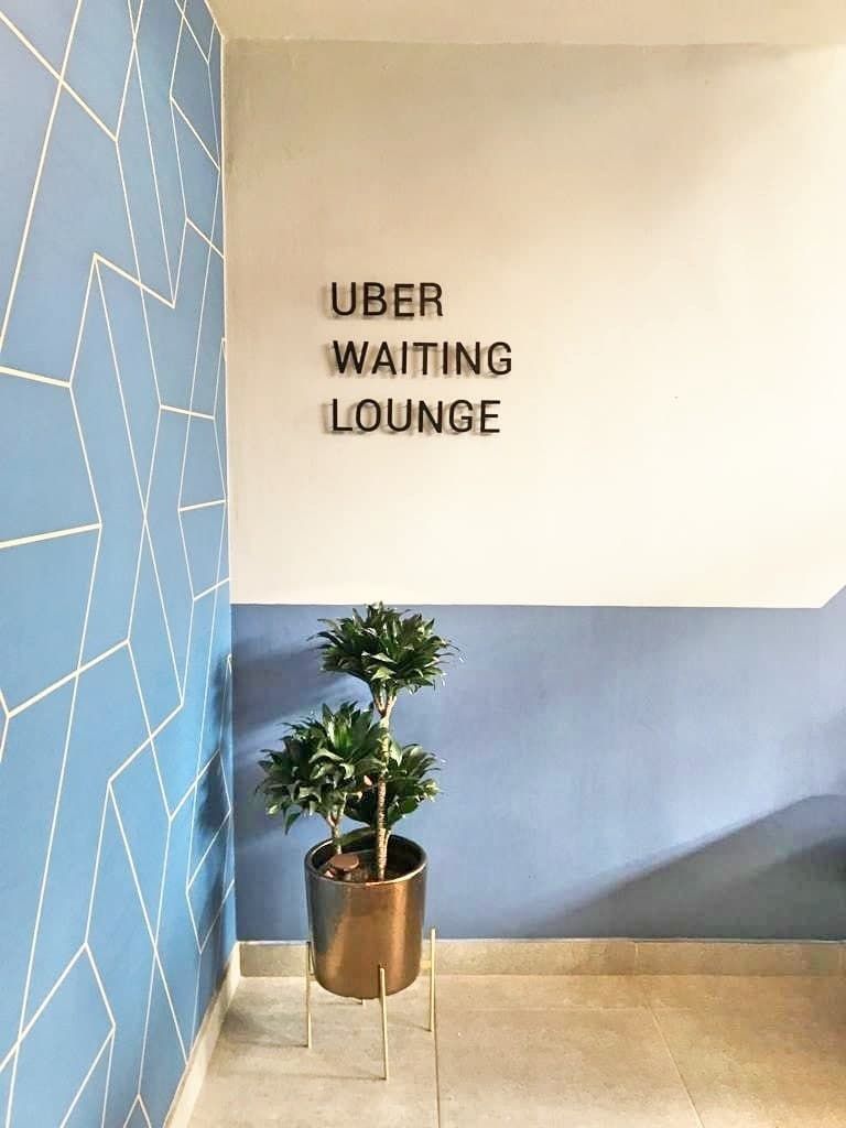 A wall with the text "UBER WAITING LOUNGE" and a potted plant.