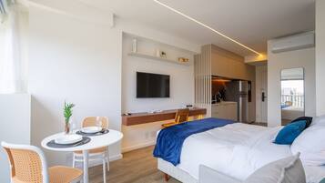 Quarto de hotel moderno com uma cama, uma mesa de jantar com cadeiras, uma cozinha e uma TV fixada na parede.