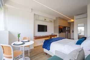 Een moderne hotelkamer met een bed, een eettafel met stoelen, een keukenhoek en een aan de muur bevestigde televisie.