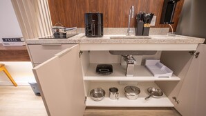 A compact kitchen with a built-in sink, a coffee maker, and various stainless steel cookware on open shelves. - For You Moema (São Paulo)