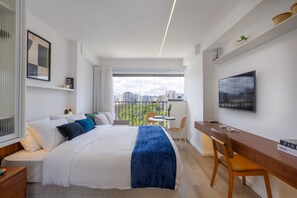 A modern hotel room with a large bed, a desk, a chair, a TV, and a balcony with a city view. - For You Moema (São Paulo)