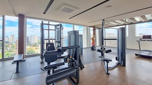 A gym with various exercise equipment, large windows, and a city view. - For You Moema (São Paulo)