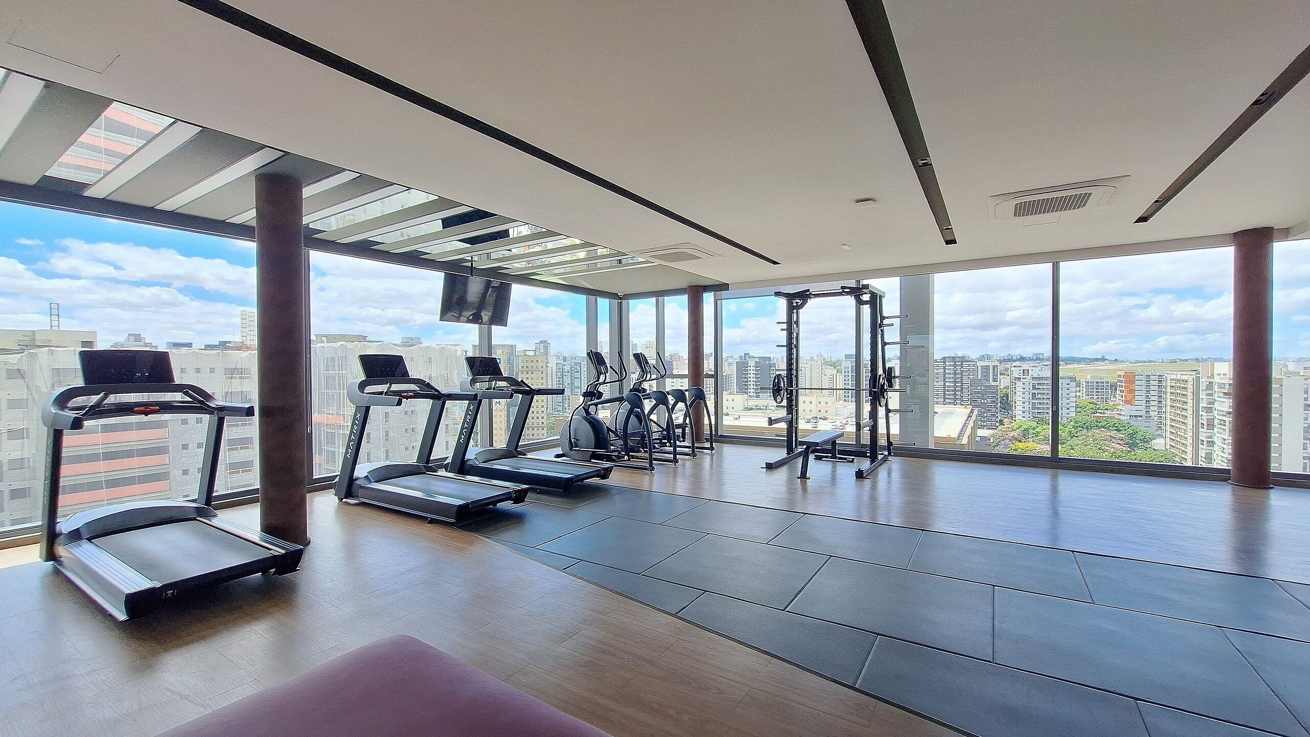 Et moderne fitnesscenter med løbebånd, crosstrainere og styrkeløftningsudstyr, store vinduer med udsigt over byen.