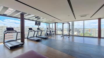 Et moderne fitnesscenter med løbebånd, crosstrainere og styrkeløftningsudstyr, store vinduer med udsigt over byen.