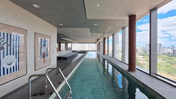 En lang, indendørs swimmingpool med udsigt over byen, liggestole og moderne arkitektur.