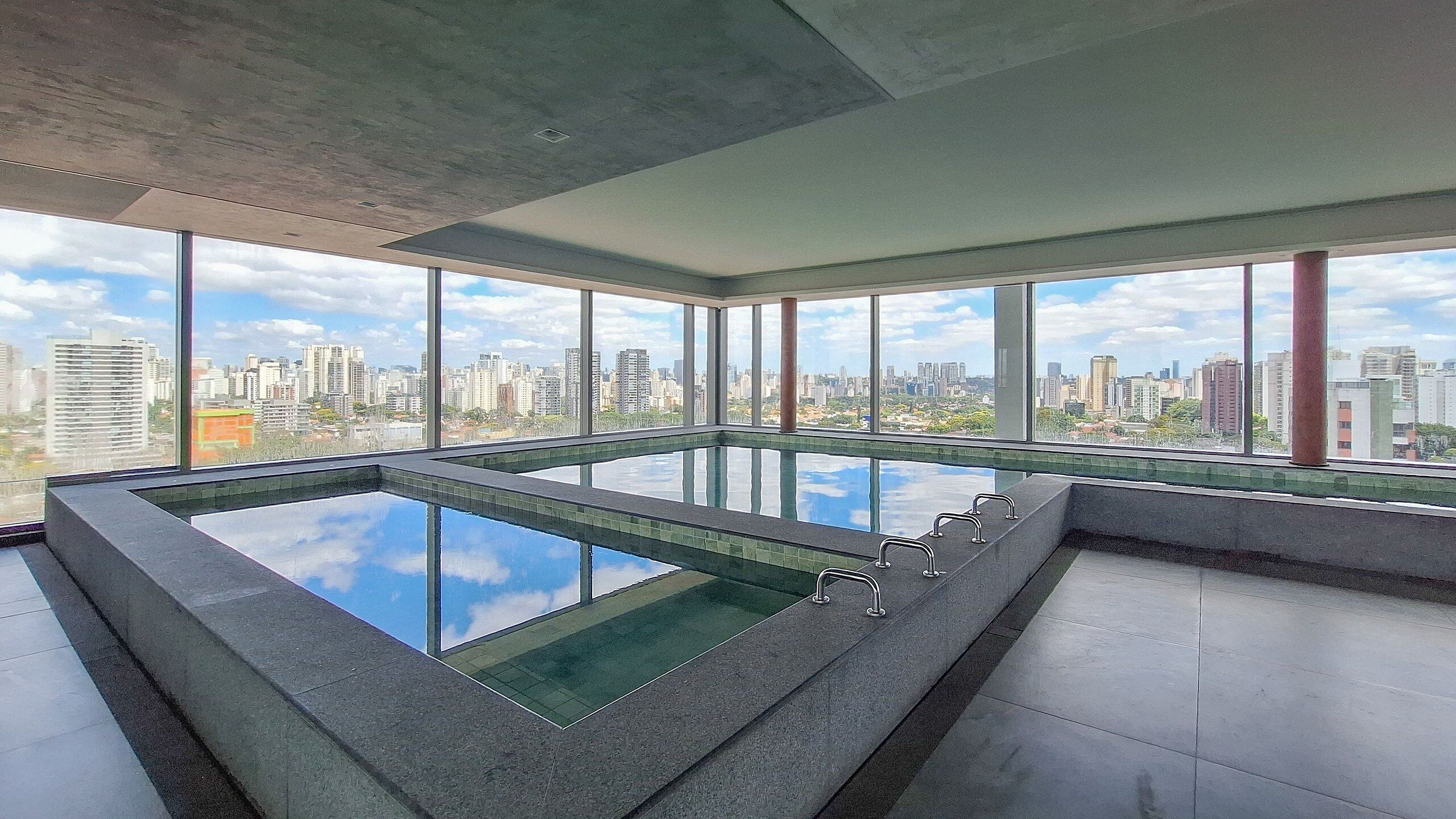 Piscina interior moderna com vista para a cidade, amplas janelas e design minimalista.