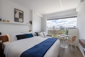 A modern hotel room with a large bed, a balcony with a dining area, and a city view. - For You Moema (São Paulo)