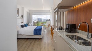 A modern hotel room with a bed, a small dining area, a kitchenette, and a large window offering a city view. - For You Moema (São Paulo)
