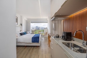 A modern hotel room with a bed, a small dining area, a kitchenette, and a large window offering a city view. - For You Moema (São Paulo)