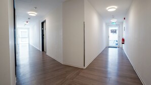 A long, narrow hallway with wooden flooring and white walls. There are doors on both sides, and a fire extinguisher is mounted on the wall. - We rooms Shortstay  (Karben)