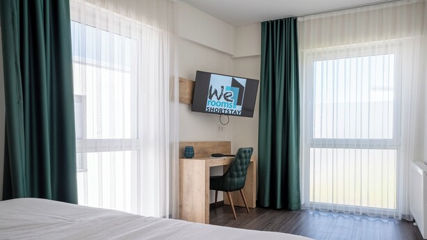 Hotelkamer met een bed, bureau, stoel en een televisie waarop 'We rooms SHORTSTAY' staat.