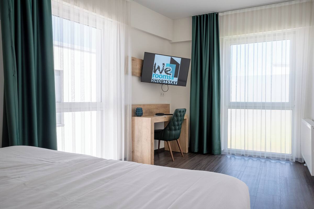 Hotelkamer met een bed, bureau, stoel en een televisie waarop 'We rooms SHORTSTAY' staat.