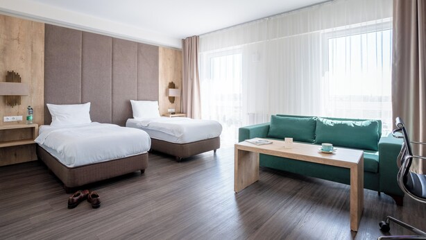 A hotel room with two beds, a green sofa, a wooden coffee table, and a view of the city through large windows. - We rooms Shortstay  (Karben)