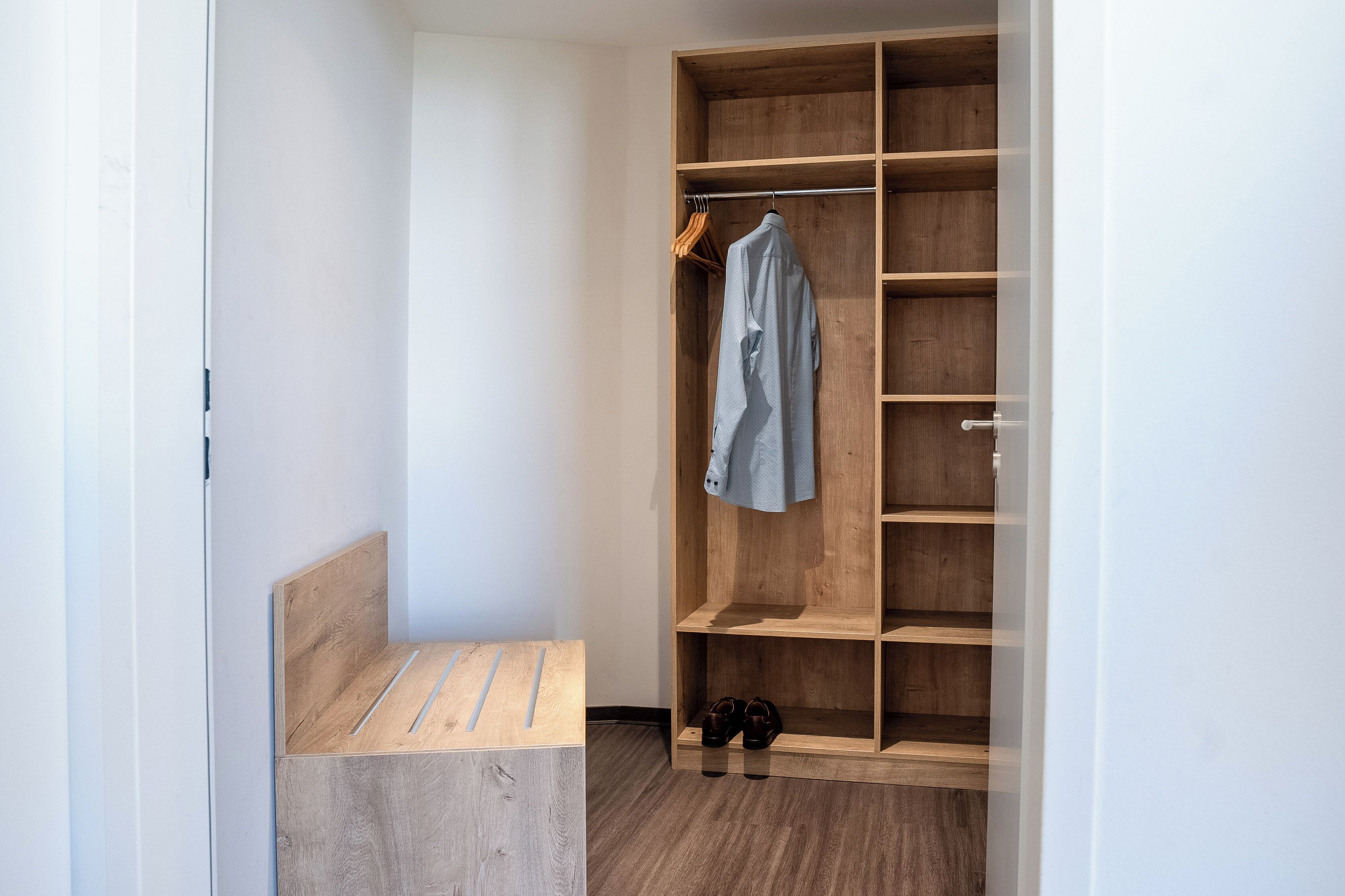 A walk-in closet with wooden shelves and a bench.