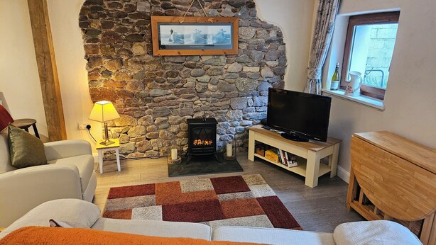 Ein gemütliches Wohnzimmer mit Steinwand, Kamin, Fernseher auf Holzständer und Fenster mit Aussicht.
