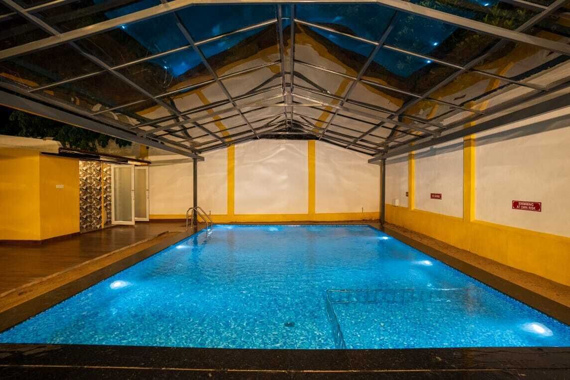 Une piscine intérieure dotée d’un toit en verre, de murs jaunes et d’une eau cristalline.