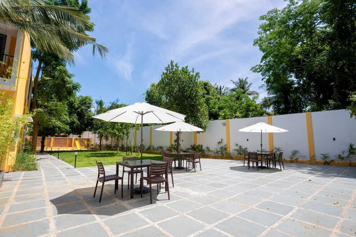 Een terras buiten met stenen vloer, tafels, stoelen en parasols.