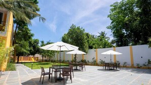 Un espace extérieur aménagé en terrasse, avec un sol en pierre, des tables, des chaises et des parasols.